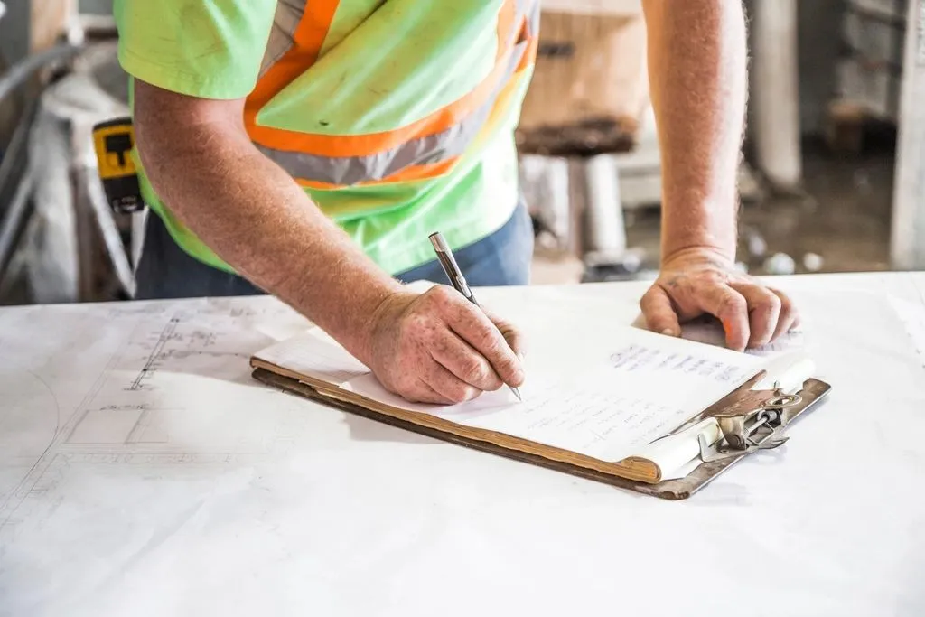 Supervisor in a high-visibility vest signing off on a clipboard