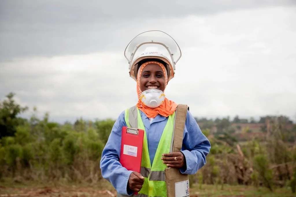 Smiling worker in a hard hat and high-visibility vest holding a clipboard